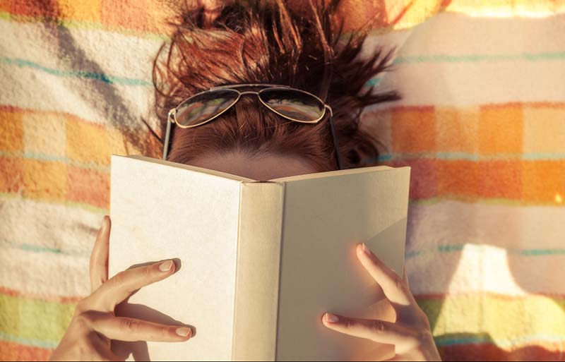Eine junge Frau liest im Sommer auf einer Decke in einem Buch, dass sie vor die Nase hält